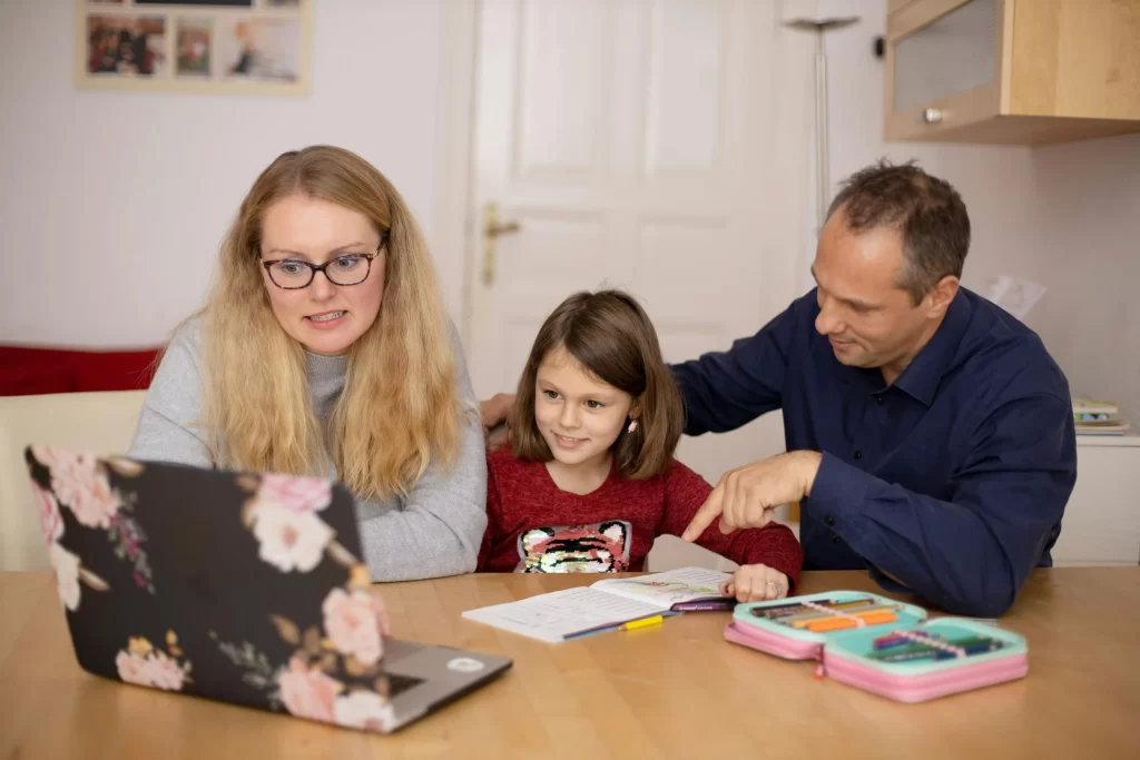 A family sitting in front of a laptop, depicting a tutoring session with an online tutor.