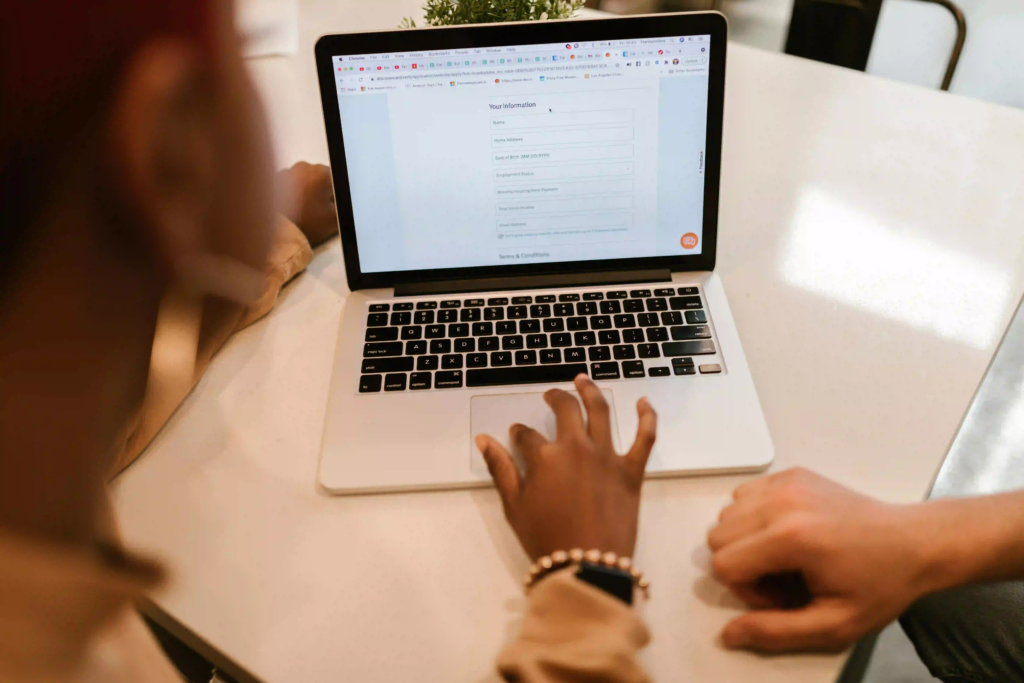 Person filling out a contact us form on a laptop, on a website, with a person nearby.
